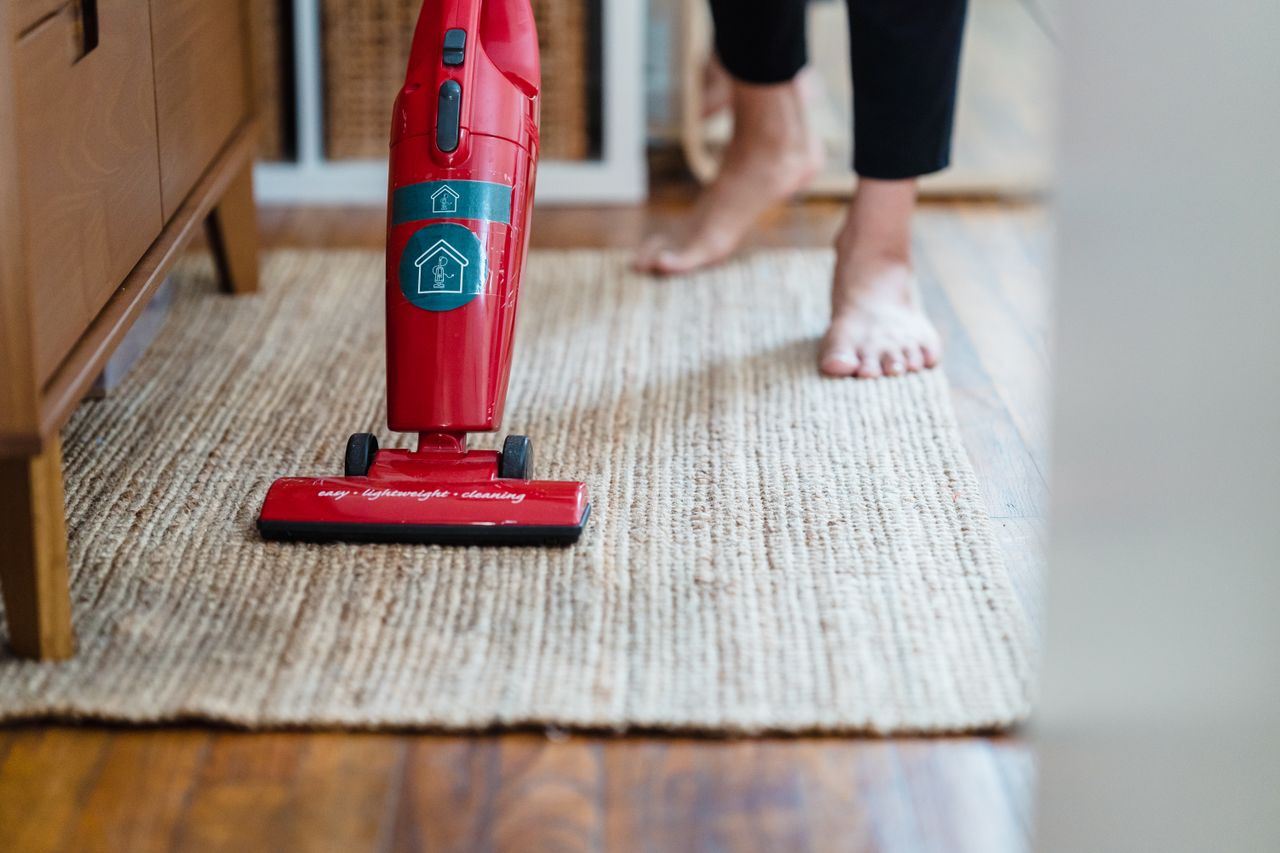home-img A red vacuum cleaner sits on a carpet in a stylish home setting, with the user barefoot.